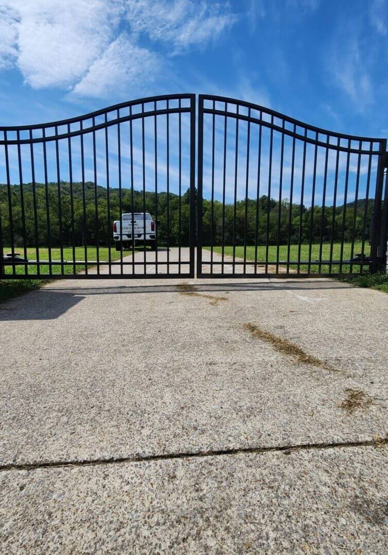 Black metal gate with stone pillars, driveway.